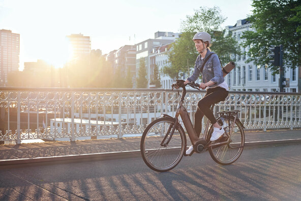 A woman riding an eBike over a bridge through the city