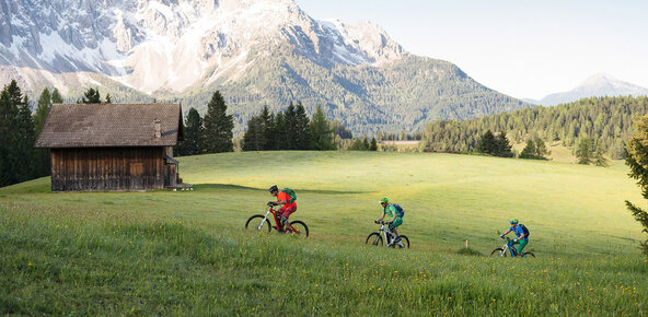 Three eBike riders on a grassy trail with snowy mountains in the background
