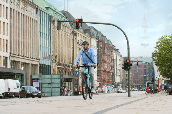 Video-Standbild zeigt Mann mit eBike-Helm, der auf einem hellblauen Pedelec durch die Hamburger City fährt