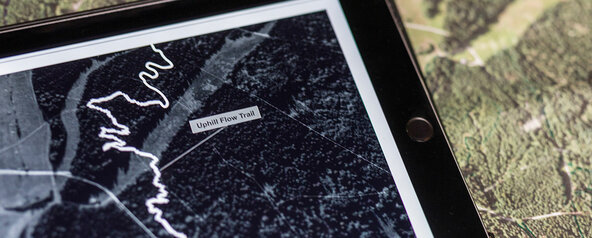 Blick auf ein Smartphone, das auf einer Geländekarte den "Uphill Flow Trail" für eBiker zeigt