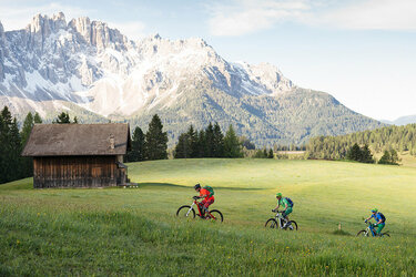 Three eBike riders on a grassy trail with snowy mountains in the background